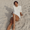 A girl seated on a  sand worn her Conscious Club White T-Shirt